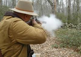Man shooting a black powder rifle in the woods.